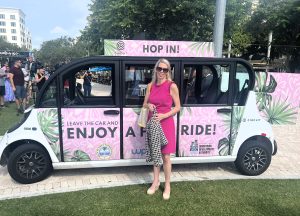 TPA Governing Board Member and City of West Palm Beach Commissioner, Christy Fox wearing a bright pink dress and posing in front of a pink local rideshare vehicle in downtown West Palm Beach