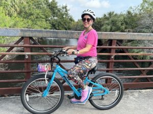 TPA Governing Board Member and City of Boca Raton Deputy Mayor, Yvette Drucker on a bicycle which is stationary on a bridge and wearing bright colors and a helmet